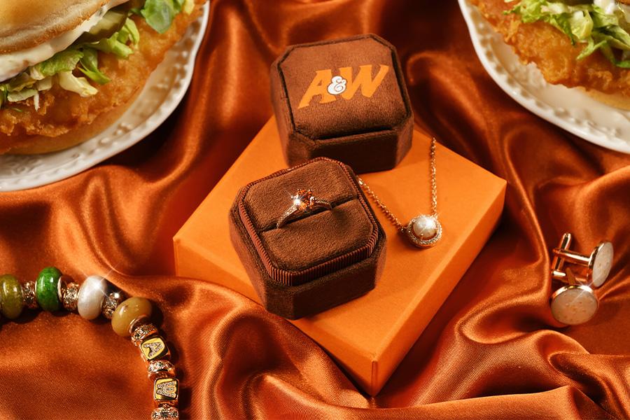 Orange diamond ring in a brown box, charm bracelet, and a necklace surrounded by two Cod Sandwiches