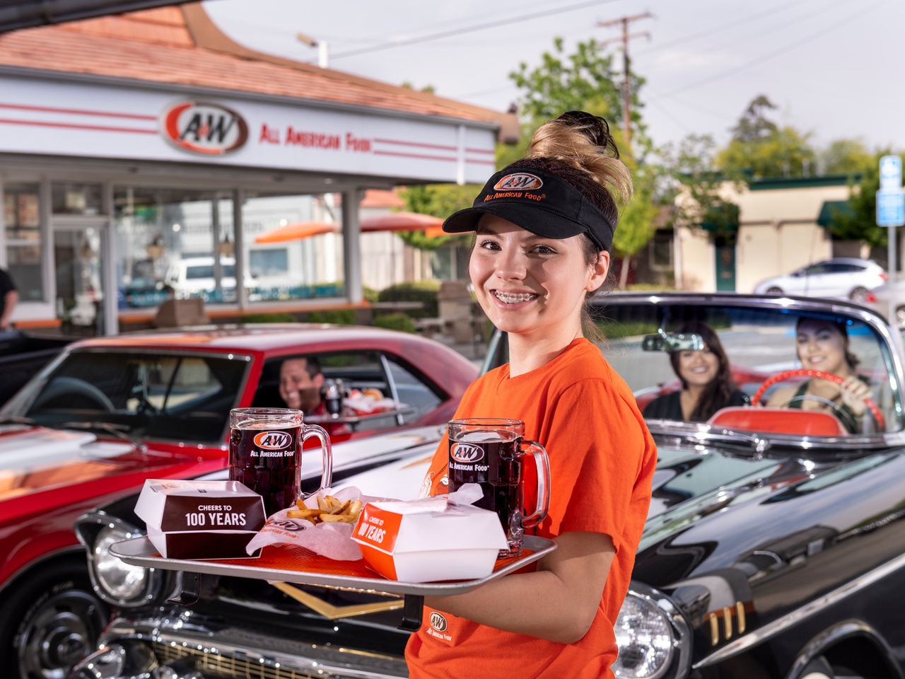 A&W Restaurant team member holding tray of food and mugs of A&W Root Beer.