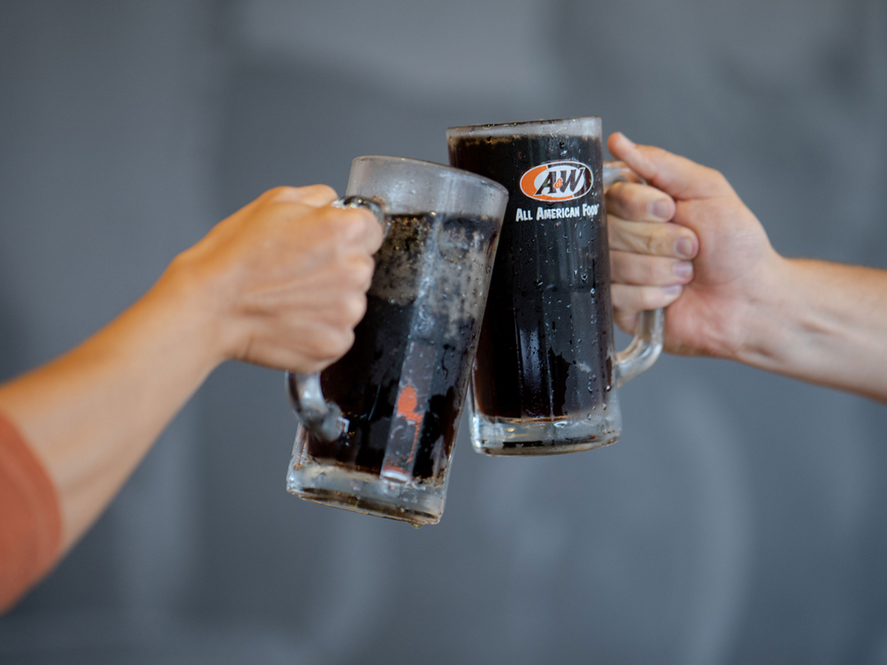 Two people clinking mugs of A&W Root Beer together
