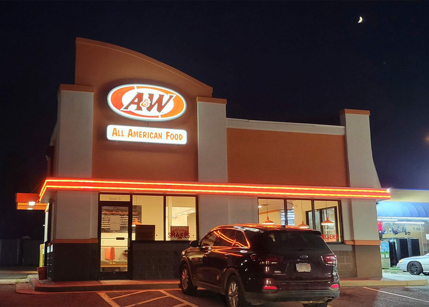 Exterior photo of an A&W Restaurant convenience store location at nighttime. A van is parked at the front of the building.