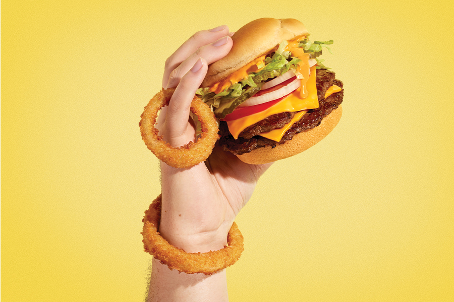 Hand holding a Double Papa Burger and Onion Rings on a yellow gradient background