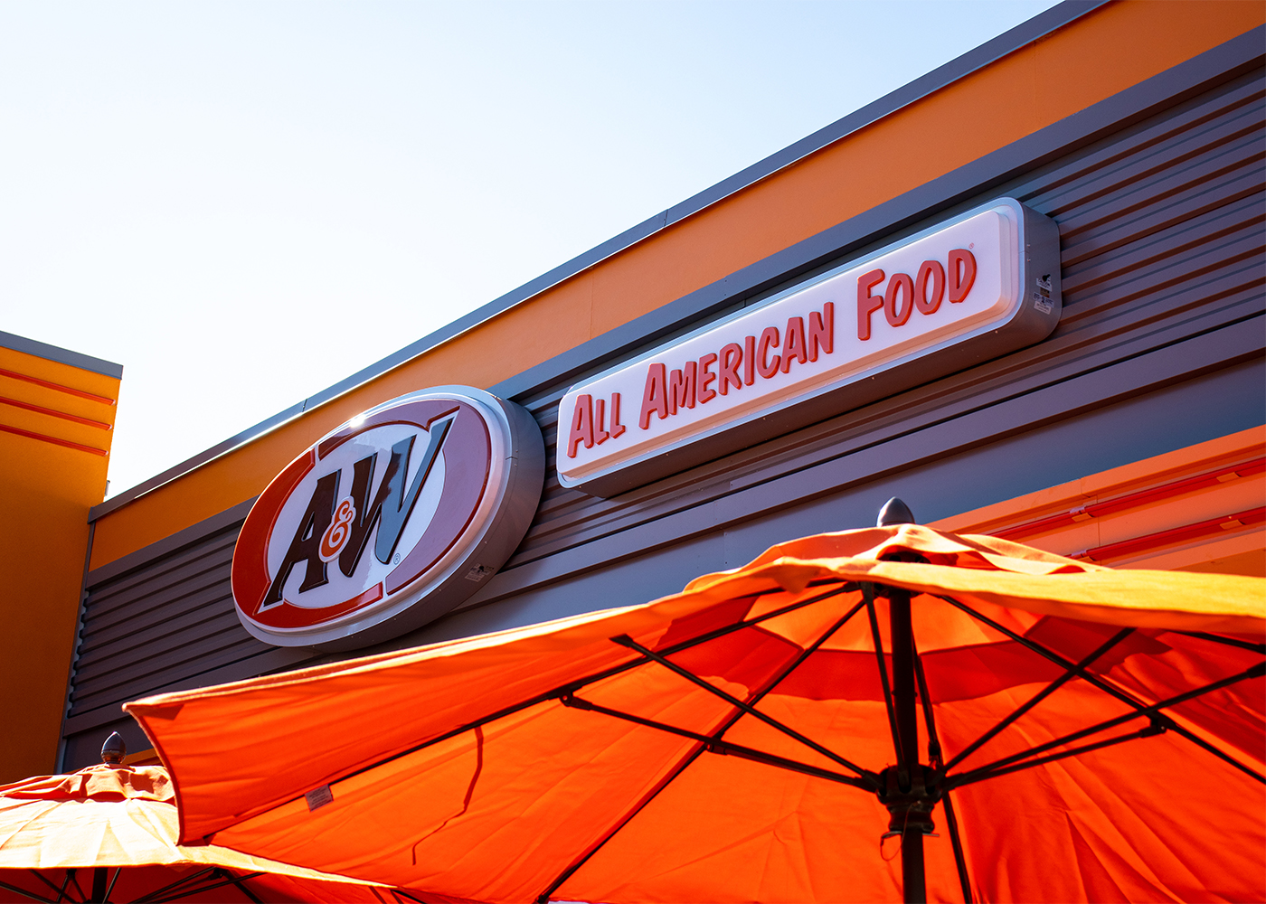 Exterior photo of the top of A&W Restaurant sign with an orange umbrella in the foreground.