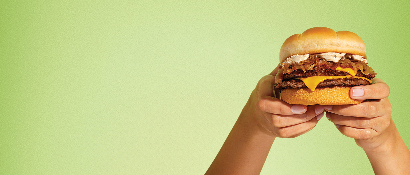 Two hands holding a French Onion Double Cheeseburger on a green background