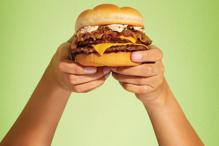 Two hands holding a French Onion Double Cheeseburger on a green background