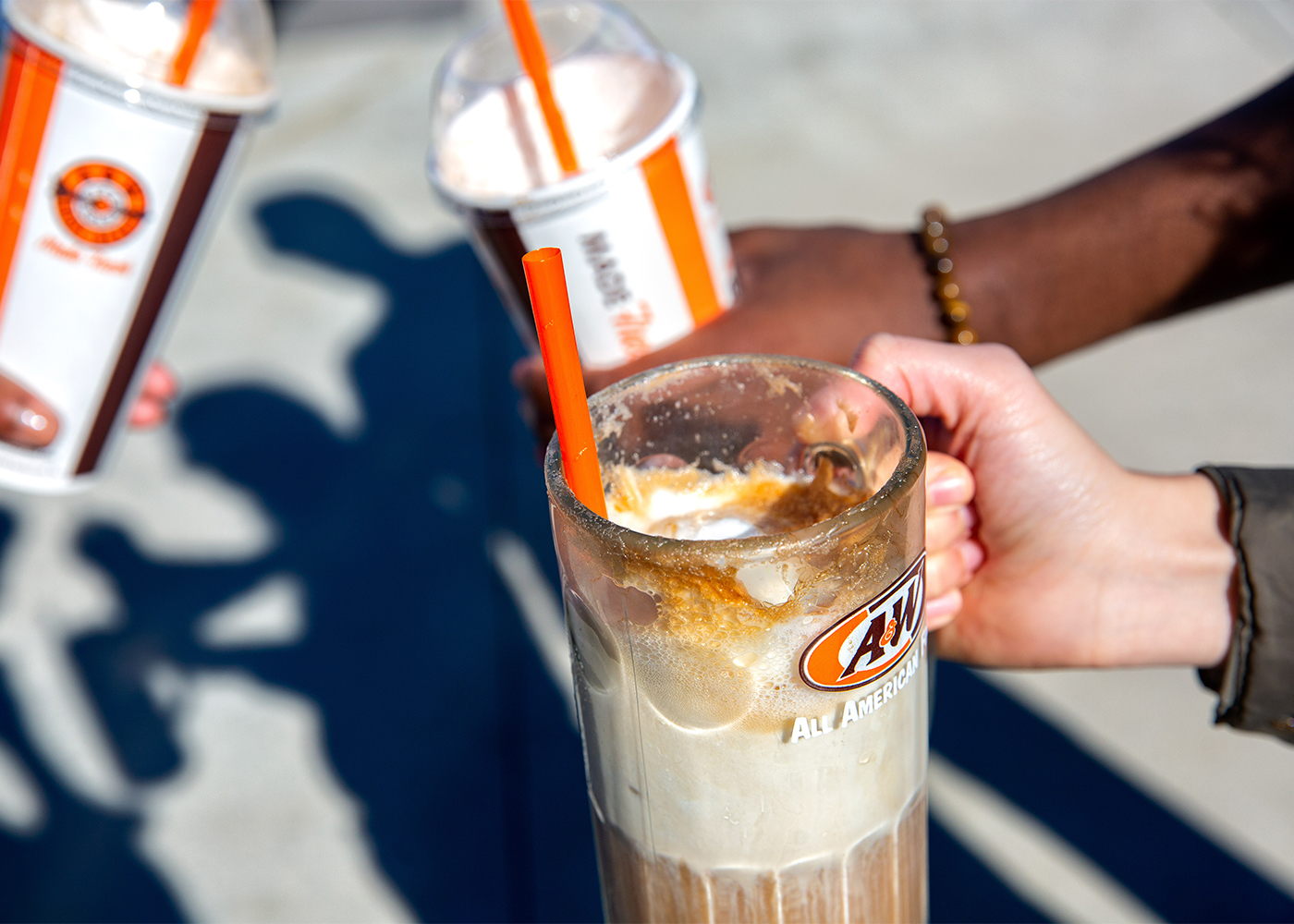 Group of people holding A&W Root Beer Floats. Two people have to-go cups and one person has a frosty mug.
