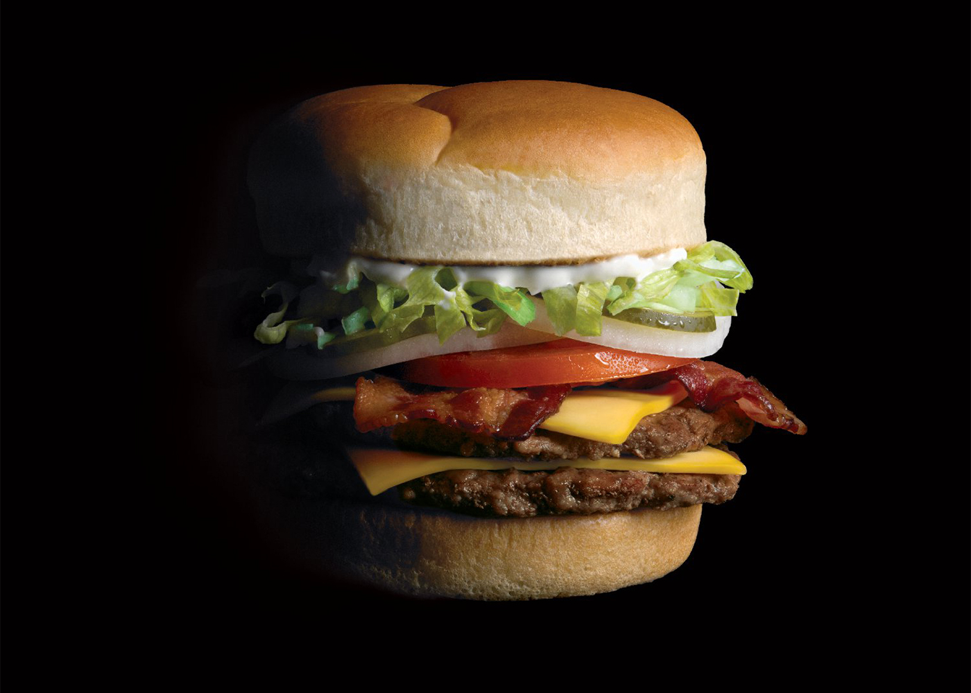 Photo of the Original Bacon Cheeseburger on a black background.