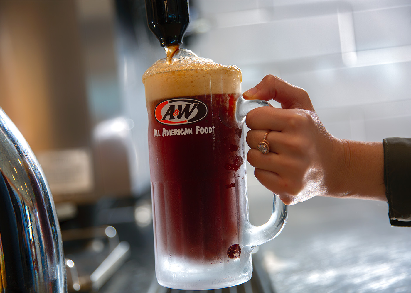 Person holding an A&W Restaurants mug as Root Beer is pouring into it.