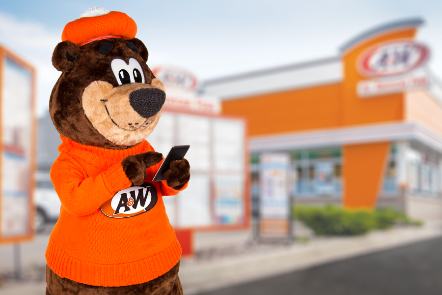 Rooty the Great Root Bear texting on a phone in front of an A&W Restaurant