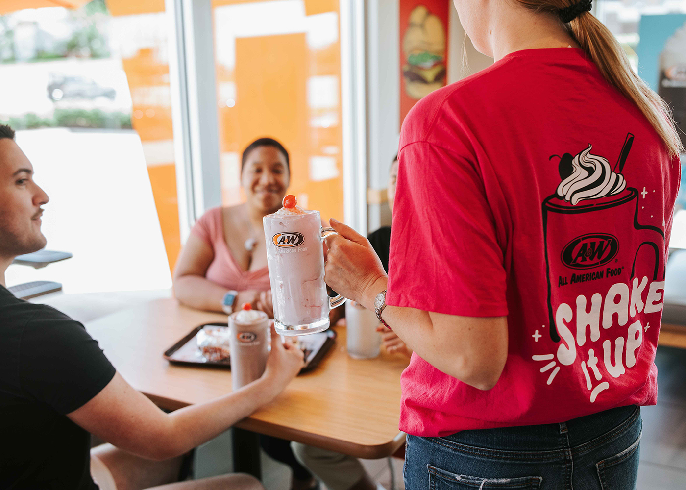 A&W Team Member bringing a Shake to a table.