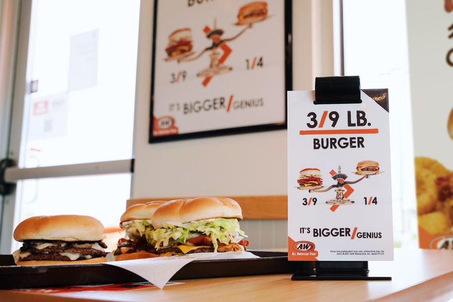 Photo of two burgers sitting on a table in an A&W Restaurant. A table tent that says 